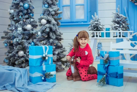 Дитяча новорічна фотосесія у фотостудії Львова, дівчинка з подарунками біля ялинки, професійний фотограф Ростислав RoStudio